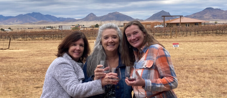 Three women smiling with glasses of wine in their hands at a winery in Southern Arizona