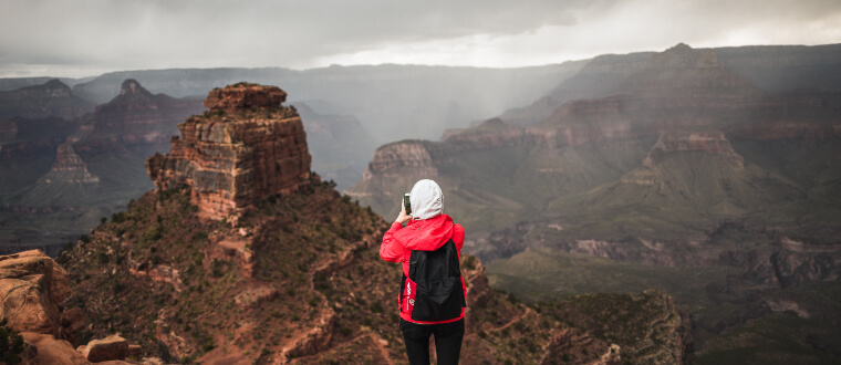 Person with hood up on a cloudy day taking a photo of the mountain landscape
